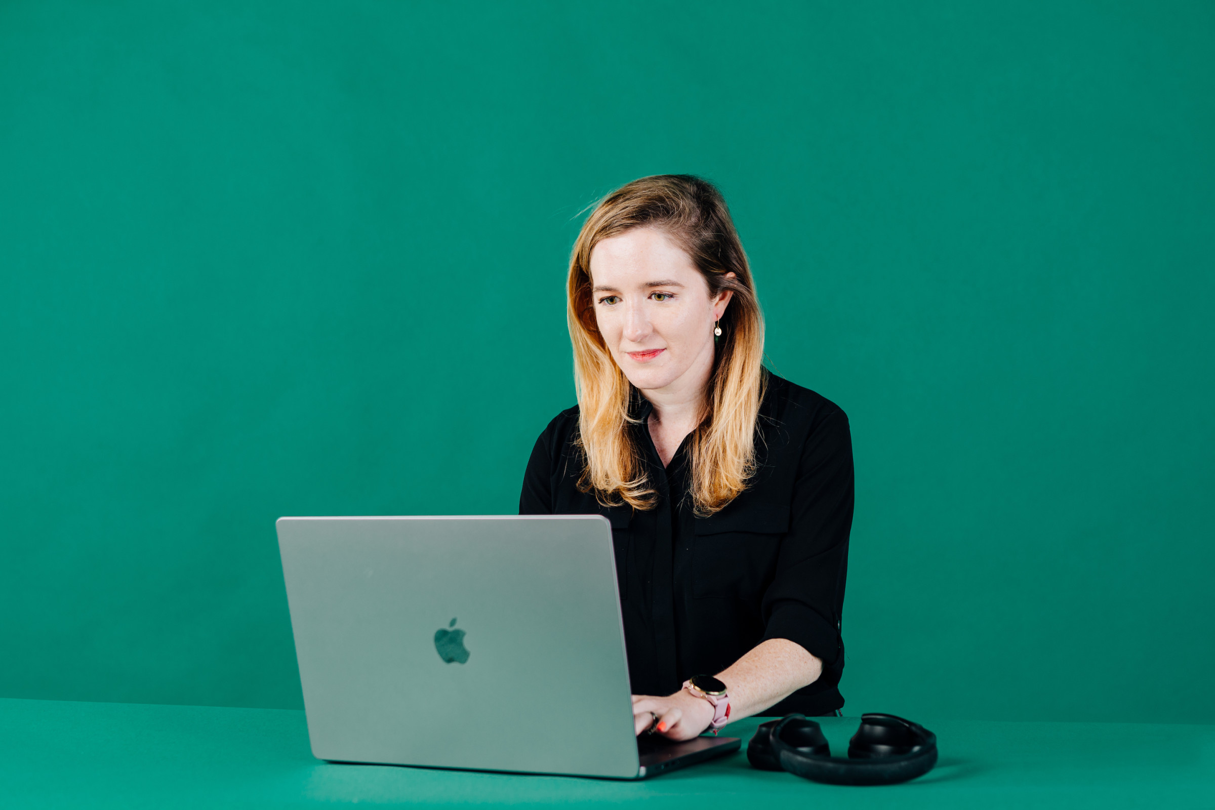 Author Keeley sitting at her laptop with her headphones against a kelly green backdrop
