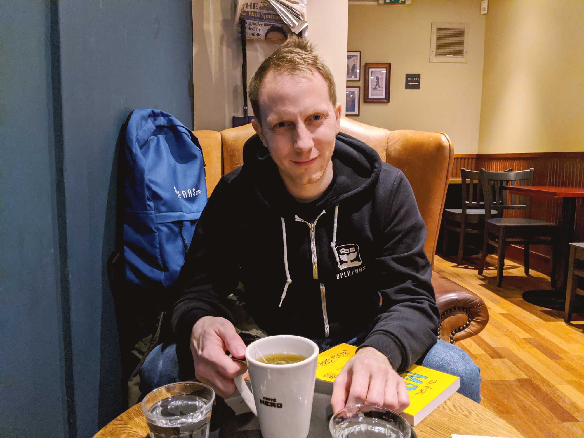 Photo of Alex Ellis at a cozy coffee shop, wearing an OpenFaaS branded hoodie.
