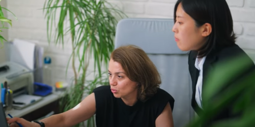 Two women in an office, discussing what's on a computer screen