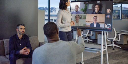 Three people in an office take part in a Teams meeting with four other people over a Surface Hub device
